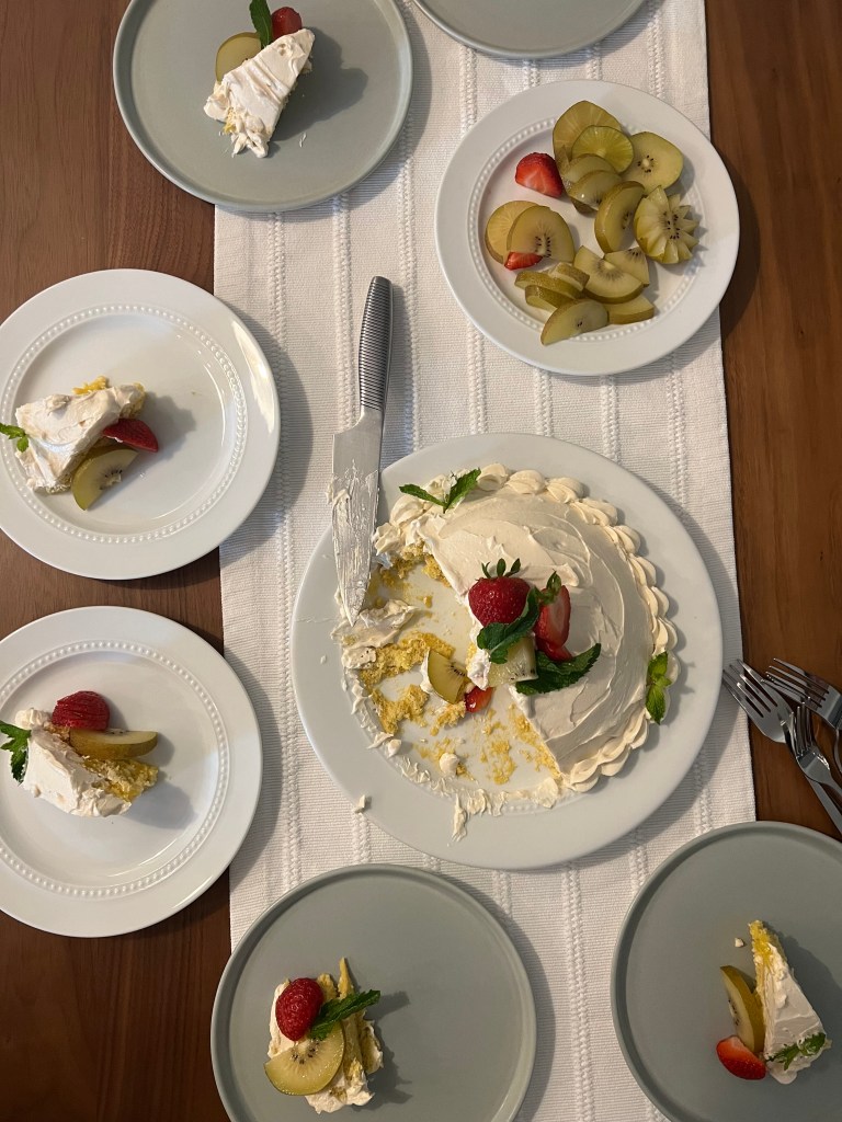 top-down view of a domed layer cake topped with fruit cut into slices on plates around the cake