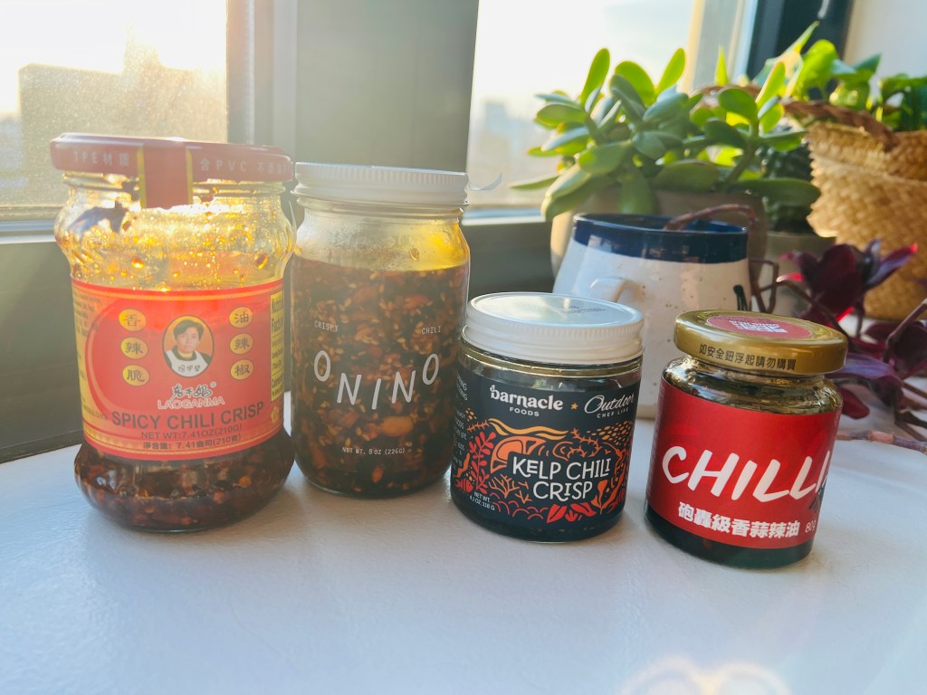 Four jars of chili crisp on a window sill 